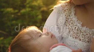 一个小孩子抱着妈妈睡着了，母女俩正走在夏天的公园里，慢镜头